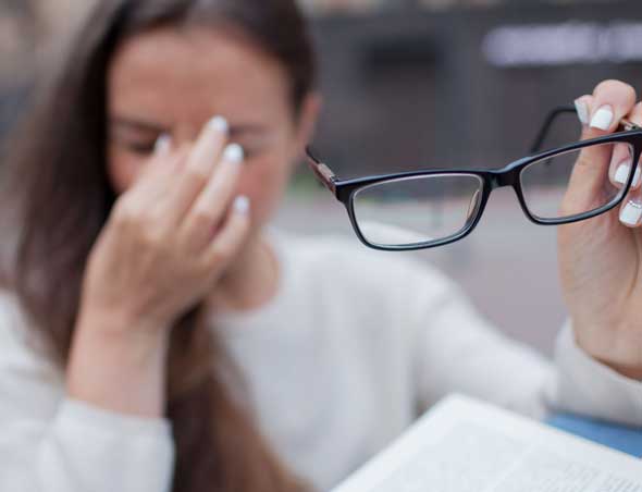 Jeune femme ayant une migraine tenant ses lunettes à distance